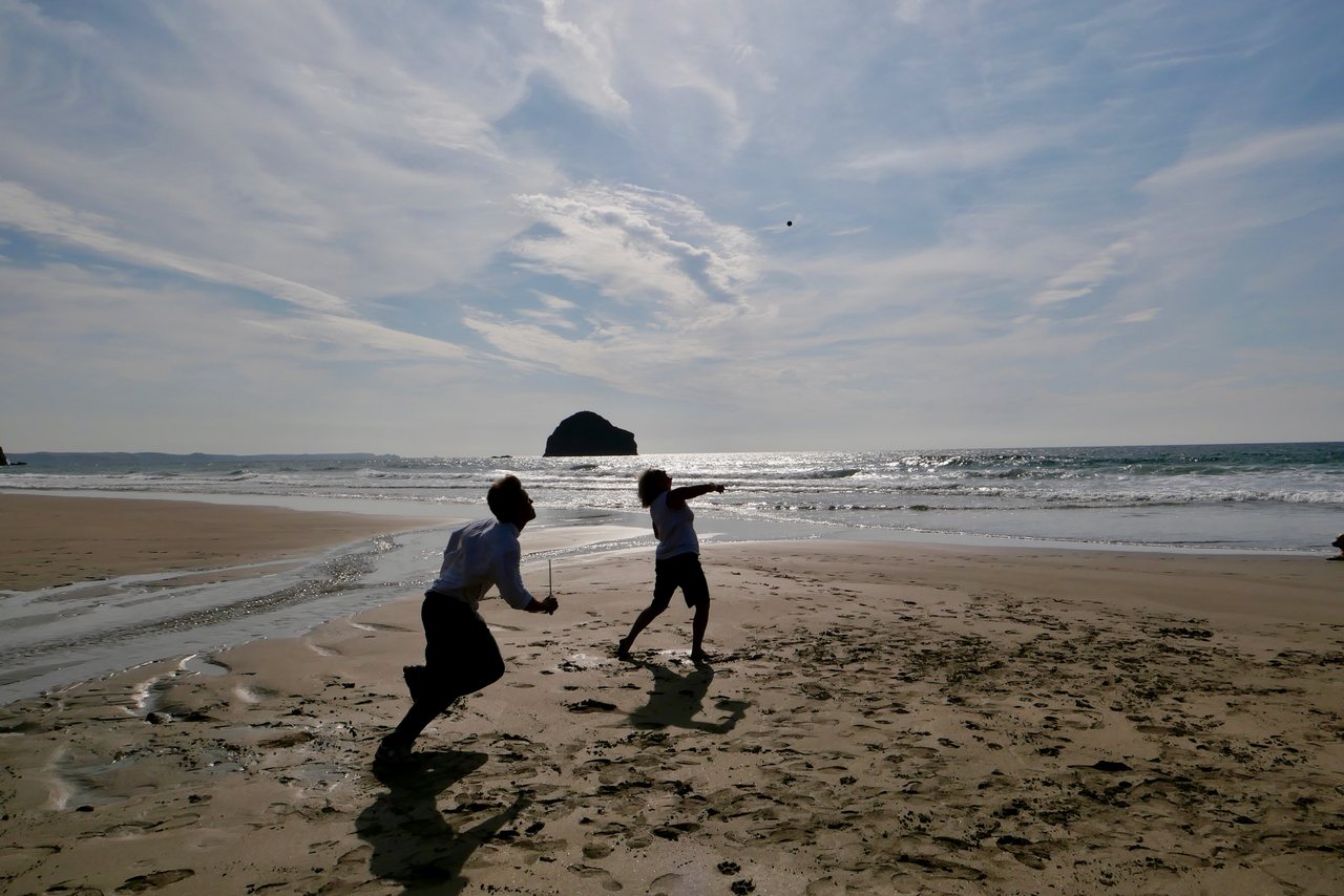 Beach Game. Two figures playing on the sand, a rock out at sea.