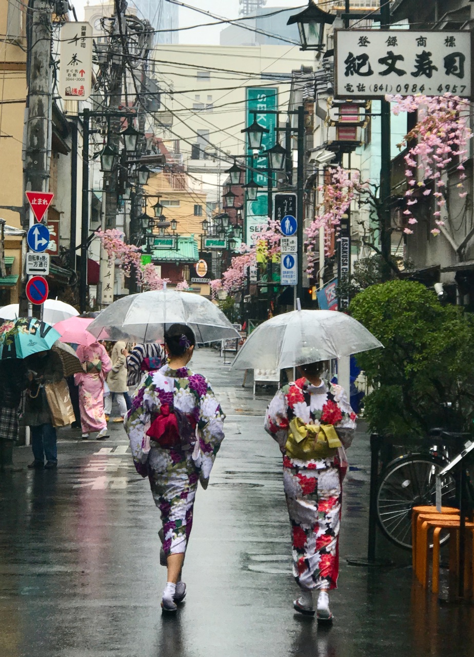 Kimonos and Umbrellas. Two ladies in kimonos stroll through the streets sheltered from the rain by umbrellas